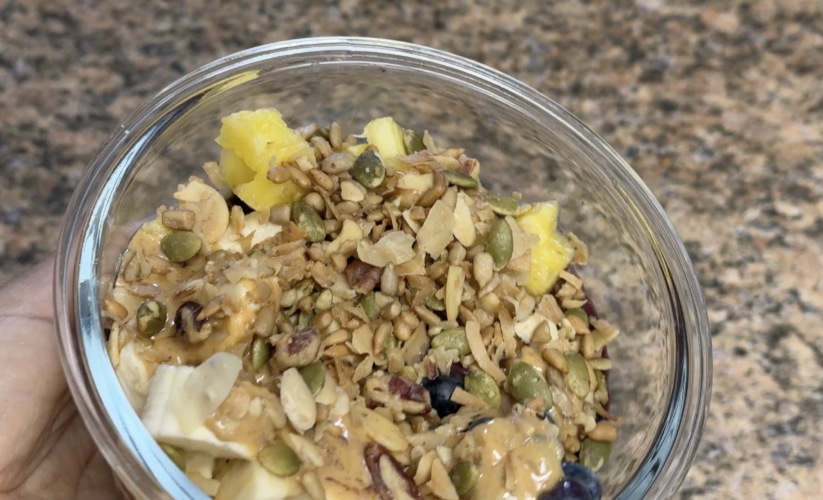 Close-up of a homemade acai bowl topped with banana, blueberries, pineapple, granola, and a peanut butter drizzle