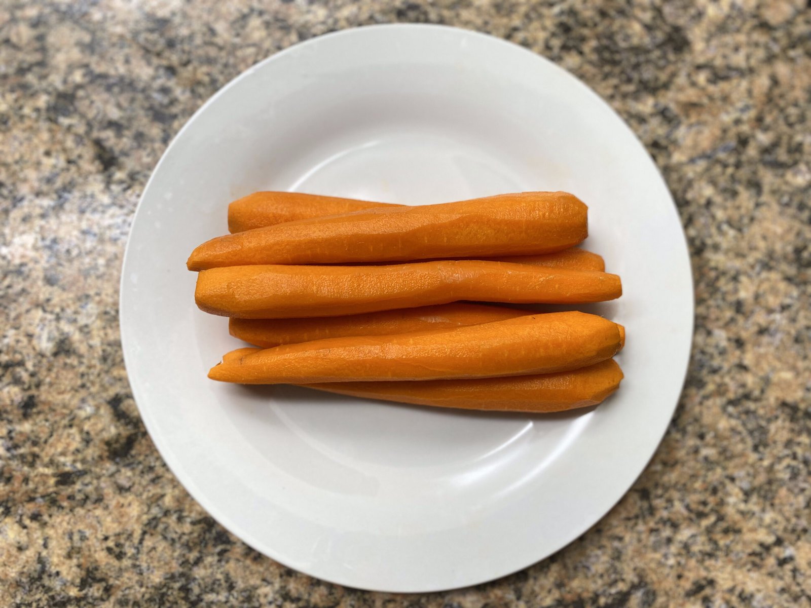 Five peeled carrots trimmed and rounded at both ends to resemble hotdogs, ready for baking