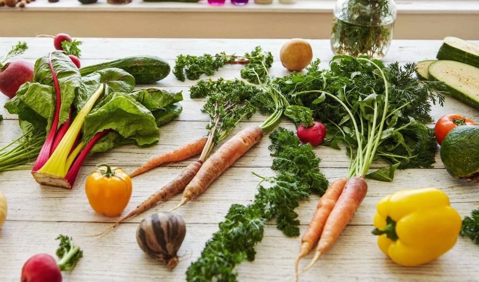 Fresh market vegetables including chard, carrots, radishes and peppers on a white wood table