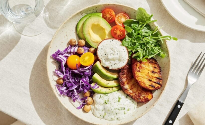 Colorful plant-based nourish bowl with avocado, tomatoes, chickpeas and purple cabbage on a linen tablecloth